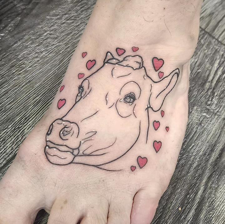 Black and grey fine line tattoo of a cow with red hearts surrounding it.