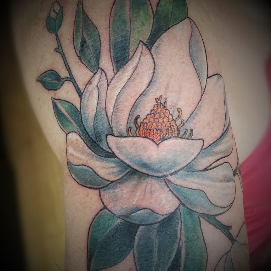 Arm tattoo of a magnolia flower in color. Book your next tattoo at Sacred Mandala Studio in Durham, NC.