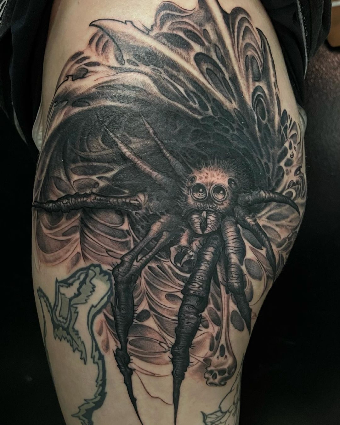 Upper thigh black and grey fine line tattoo of wolf spider with hanging skull by tattoo artist Shaine Smith.