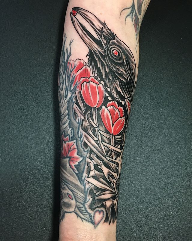 Red-eyed black crow with red tulips and pomegranate seeds. Book a custom tattoo with Chris at Sacred Mandala Studio - Durham, NC.